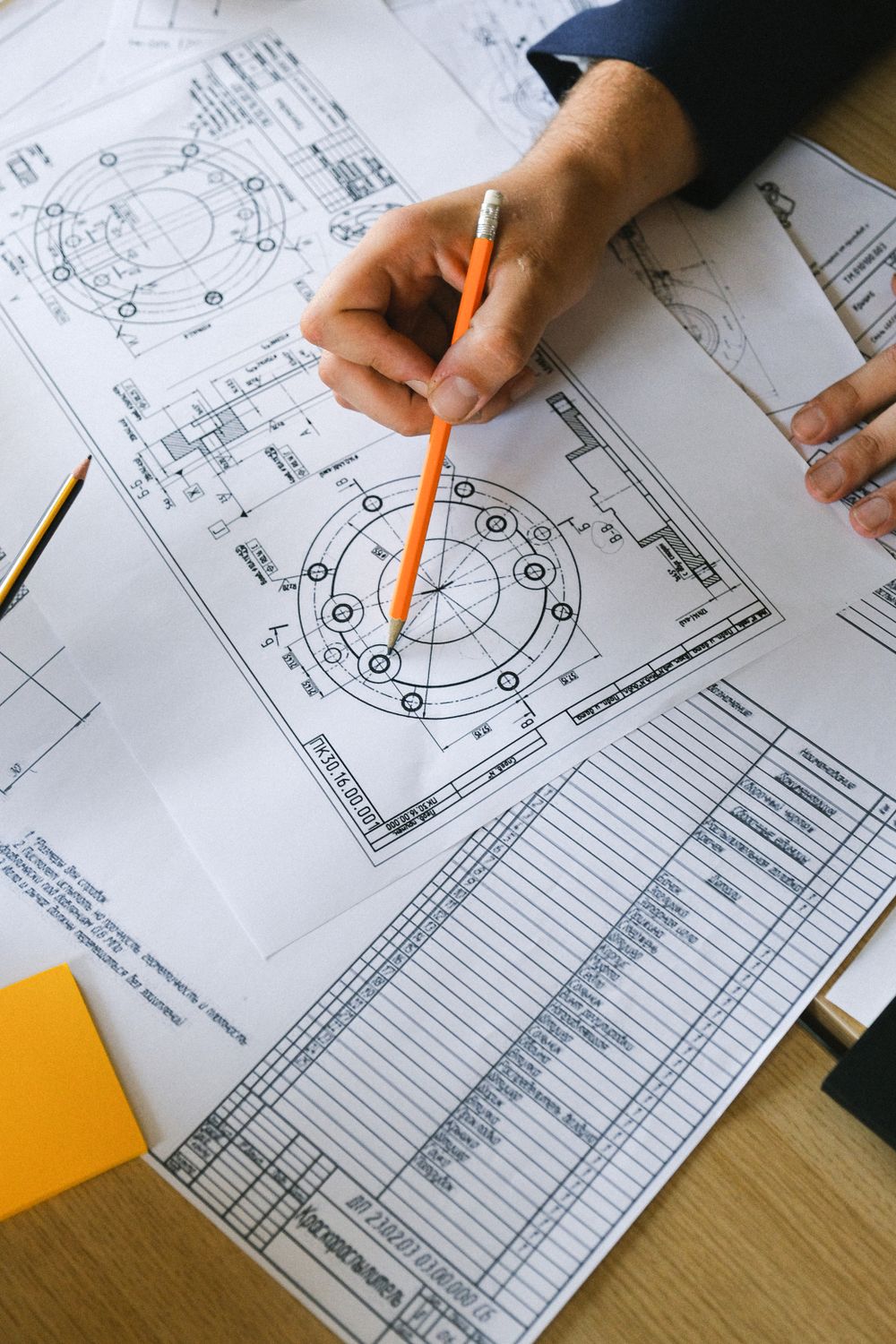 Monochrome photograph: Technical drawings being reviewed with a pencil.